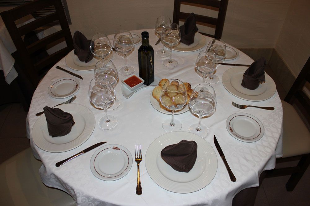 Mesa y sillas preparadas en comedor con pan y vino para varios comensales  de Restaurante Venta San José en Zafra de Záncara